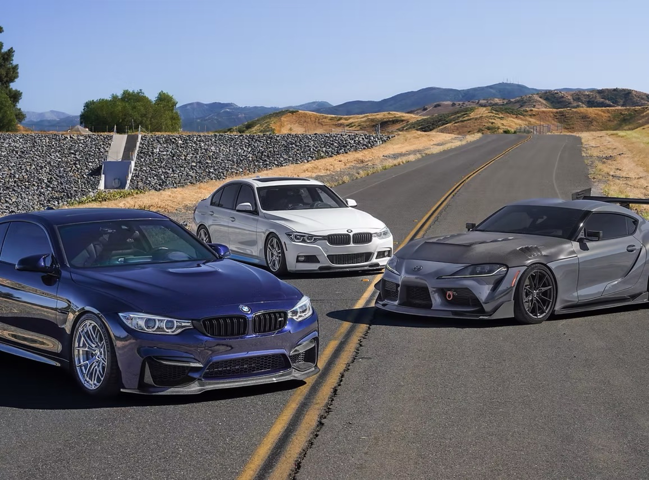 A BMW M4, BMW 3 Series, and Toyota Supra parked on a mountain road